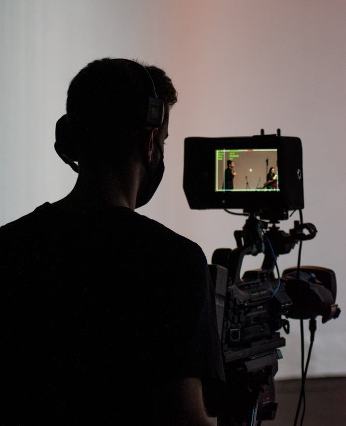 Contacto contenido audiovisual Tarragona. Silhouette of a cameraman operating professional video equipment in a studio setting.
